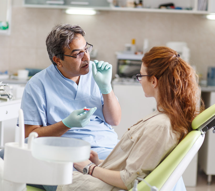 Senior male dentist in dental office talking with female patien